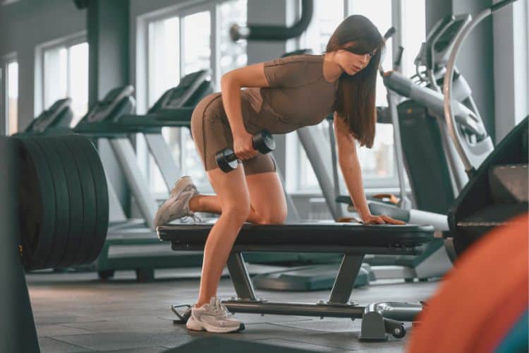 A Woman performing dumbbell bent over row during a 40-minute upper body dumbbell workout at a gym.