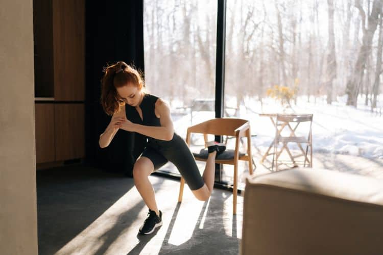 A woman performing a bodyweight squat during a 20-minute winter home workout in a cozy living room.