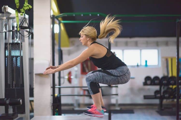 A woman performing jump squat during a 10-minute HIIT workout plan at a gym.