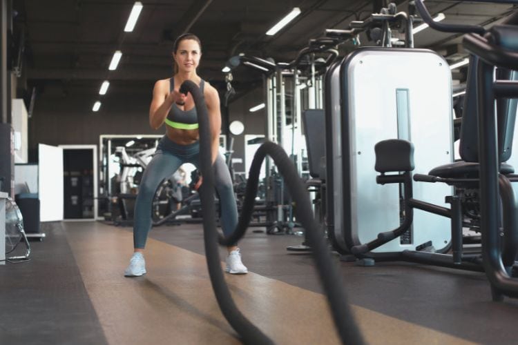 Woman performing powerful bilateral battle rope waves in a gym, demonstrating the 15-minute battle rope workout.