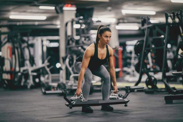 A woman smiling confidently and ready to begin the 20-minute full-body weight lifting workout at a gym.