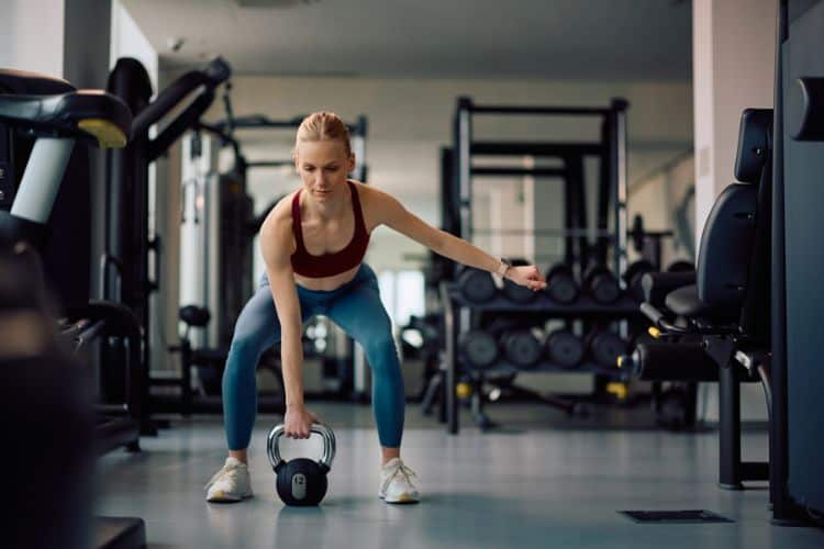 Woman performing a kettlebell swing during a 25 minute booty workout at a gym.