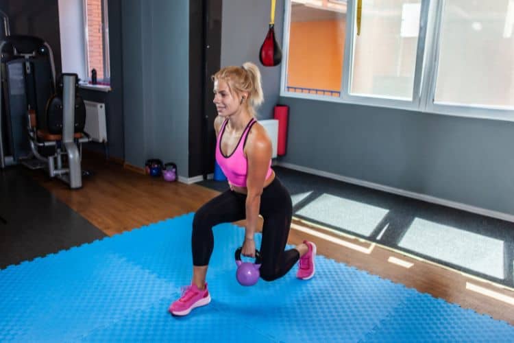 A woman performing a kettlebell reverse lunges during a 45-minute full body workout plan at a gym.