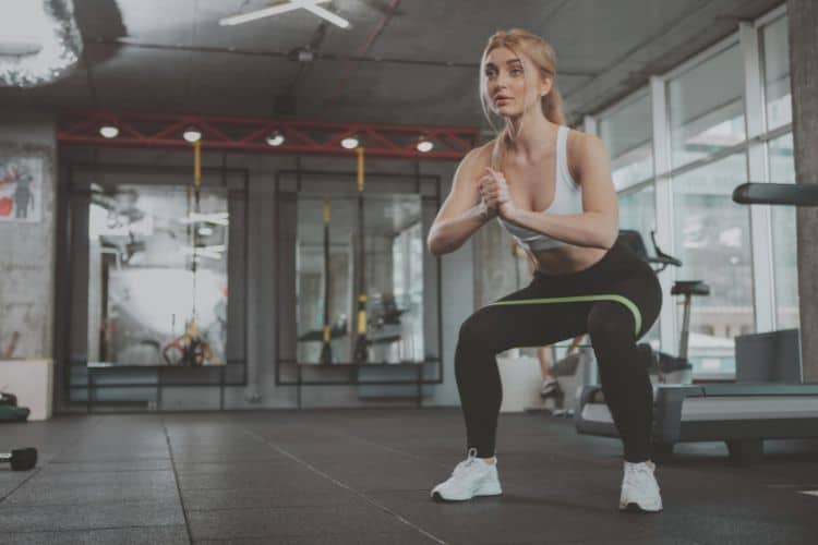 A woman performing bodyweight squat during a 15-minute full body workout in a gym.