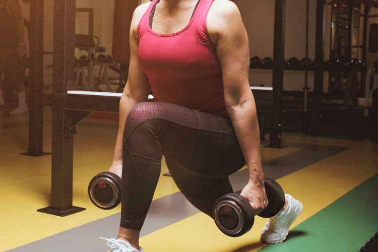 Woman performing dumbbell reverse lunges during a 10-minute over 5o dumbbell workout at a gym.