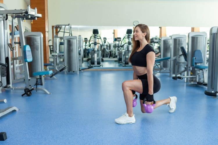 Woman performing a kettlebell reverse lunges during a 25 minute booty workout at the gym.