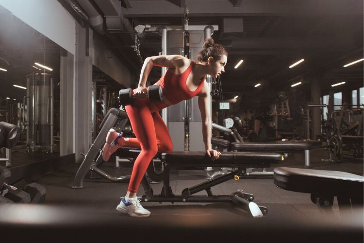 Woman in a strong bent-over dumbbell row position, back flat, targeting lats and upper back muscles during a 20 minute weightlifting dumbbell workout.
