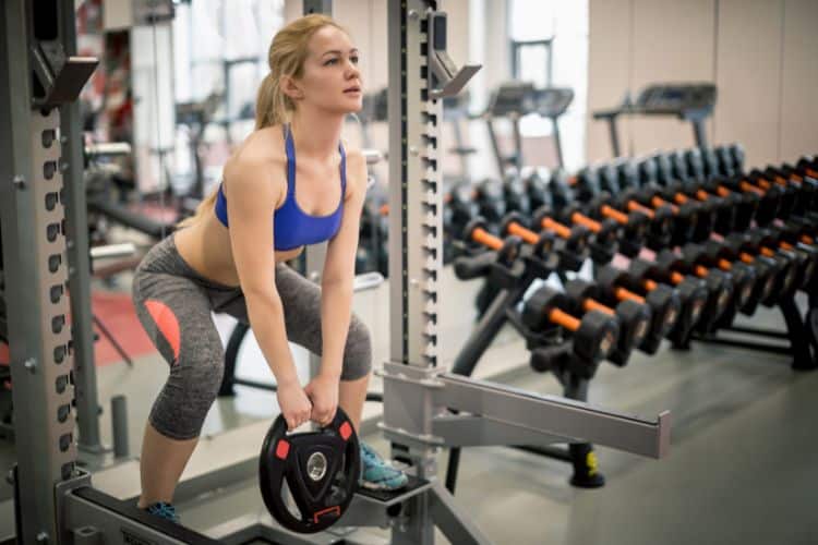 A woman performing squat with weight plate during a 5-minute full body weight plate workout.