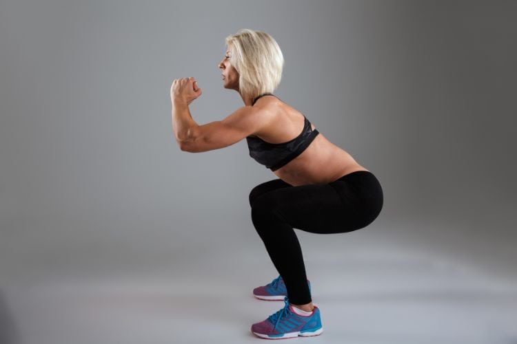 woman over 50 performing a bodyweight squat during a beginner HIIT workout for women over 50 at a gym.