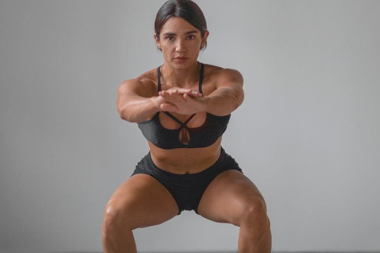 A woman performing Low-impact bodyweight squat with correct form to protect knees and build leg strength during a 5 minute Low-impact full body workout.
