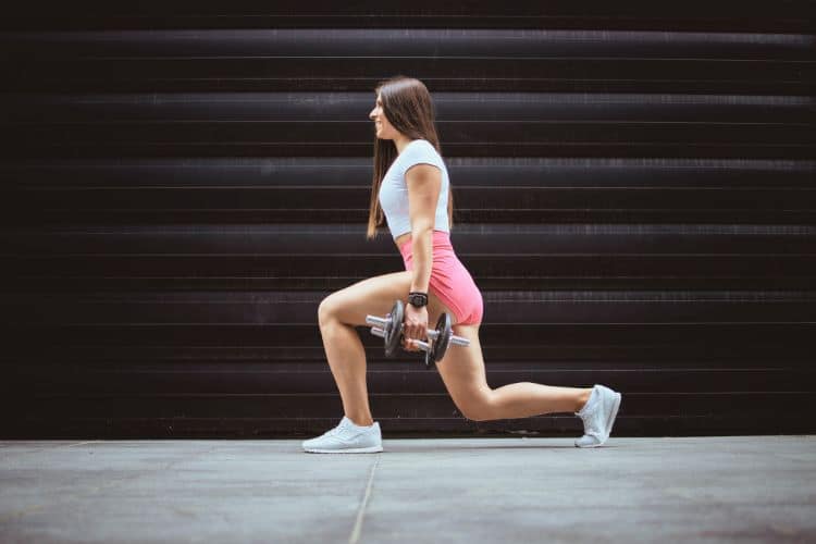 Woman performing a dumbbell reverse lunges during a 10-minute full body workout at the gym.