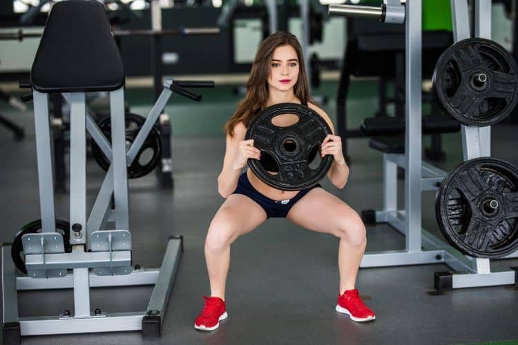 Woman performing a goblet squat with weights in a gym as part of a 15-minute full body workout with weights.