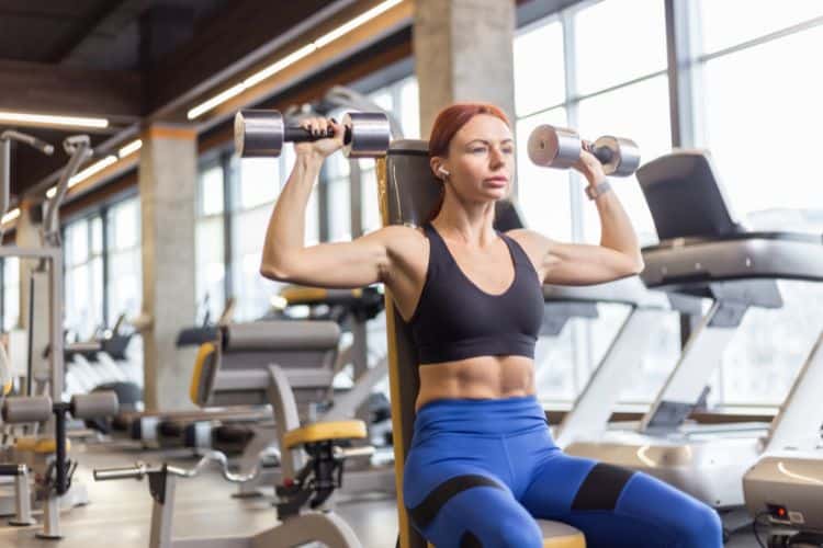 Woman performing dumbbell shoulder press in a 20-minute shoulder workout.