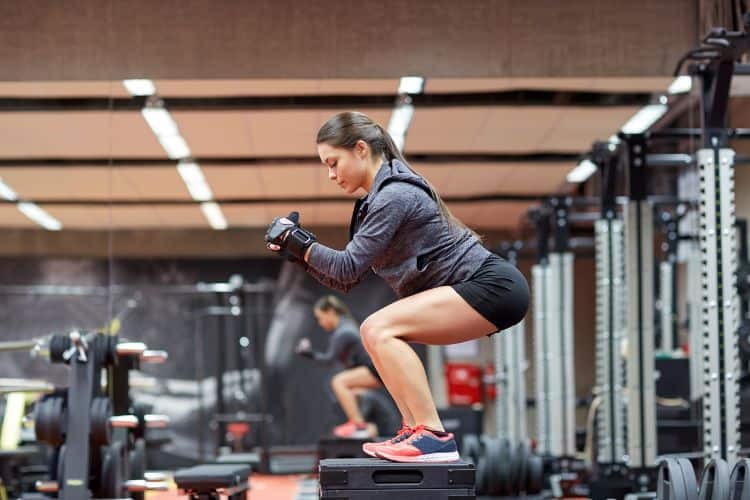 A woman performing a 30-minute box jump burpee combo workout on a plyometric box in a gym.