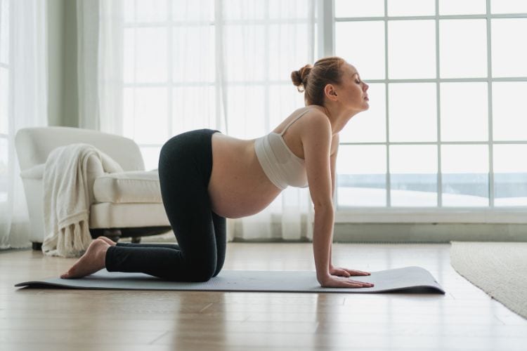 A happy woman in her third trimester safely performing a prenatal 30 minute cat-cow stretch third trimester workout on an exercise mat.