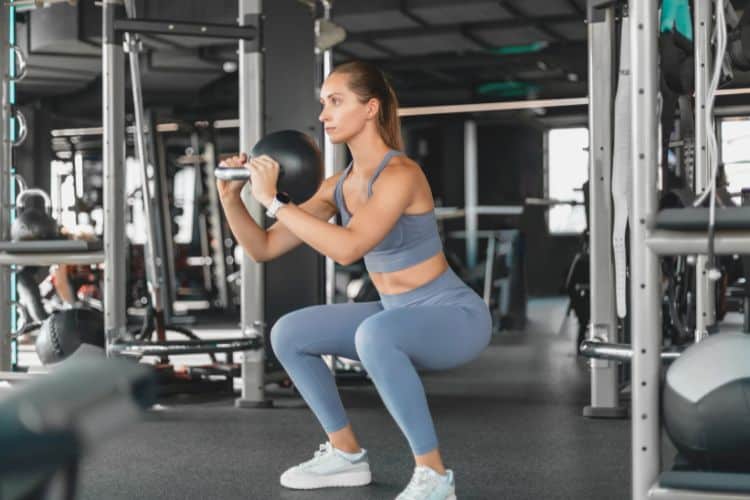 Woman performing goblet squat during a 30-minute leg resistance exercise workout at the gym.