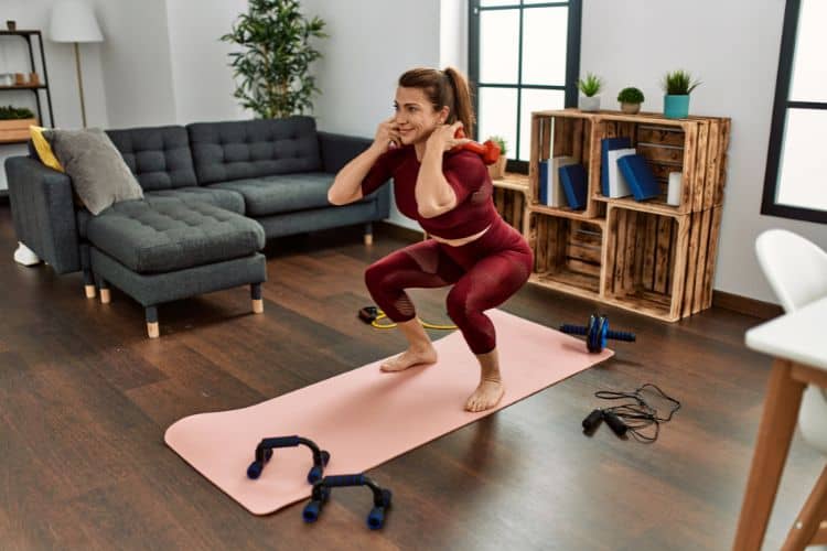 Woman performing a goblet squat with single dumbbell during 30 minute lower body dumbbell workout at home in living room.
