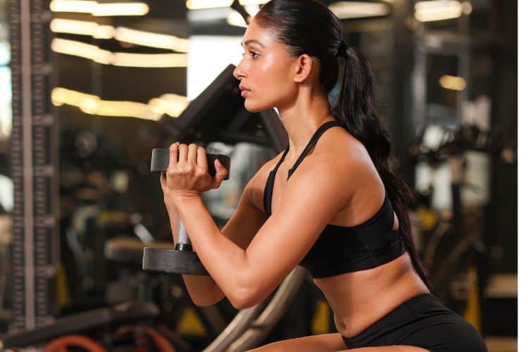 Woman performing a beginner lower body dumbbell workout holding a dumbbell in each hand during a 30-minute beginner lower body dumbbell workout.