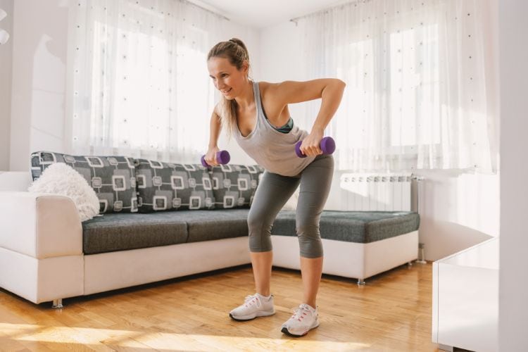 Woman performing dumbbell rows at home, demonstrating proper form for an 30 minute upper body dumbbell workout at a home.