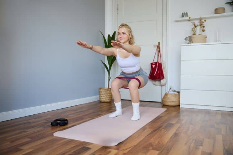 A happy new mom performing a gentle bodyweight squat in her living room during a 30-minute home workout for new moms.