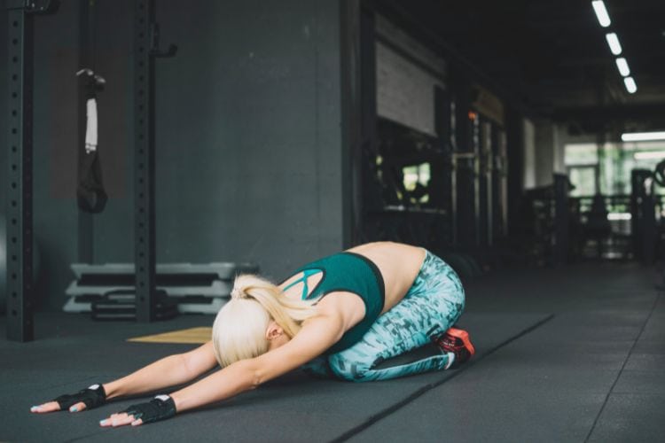 Woman performing Child’s Pose during a 15 minute morning yoga routine in a gym.