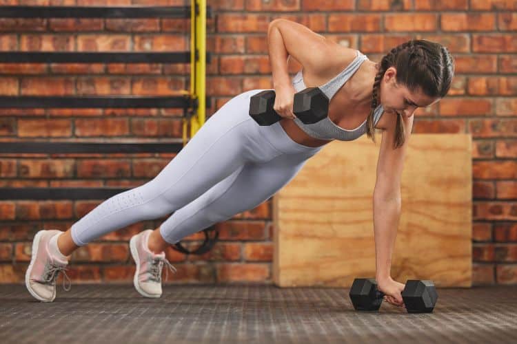 Woman performing a dumbbell renegade row during a 30 minute full body dumbbell HIIT workout in a gym.