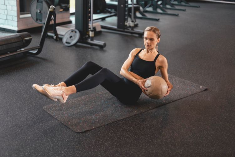 Woman performing Russian Twists with medicine ball in hand, engaging obliques for anti-lateral flexion functional ab exercises training.