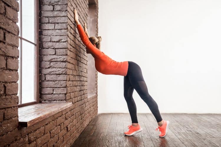 Woman doing wide-legged forward fold against a wall in a 30 minute yoga wall workout, focusing on hamstring stretch and spinal decompression.