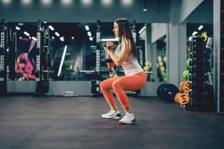 Woman performing a dumbbell squat during a one hour full body dumbbell strength workout in a gym.