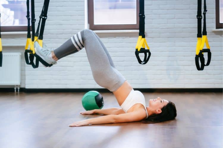 Woman performing Glute bridge core exercises with hips lifted toward the ceiling, feet flat on the floor shoulder-width apart, hands resting at sides.