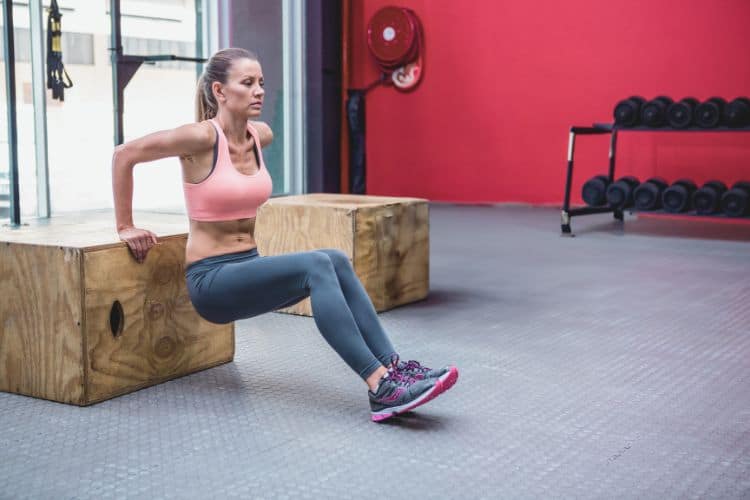Woman performing Bodyweight Triceps dips in a 45 minute full body circuit workout in the gym.