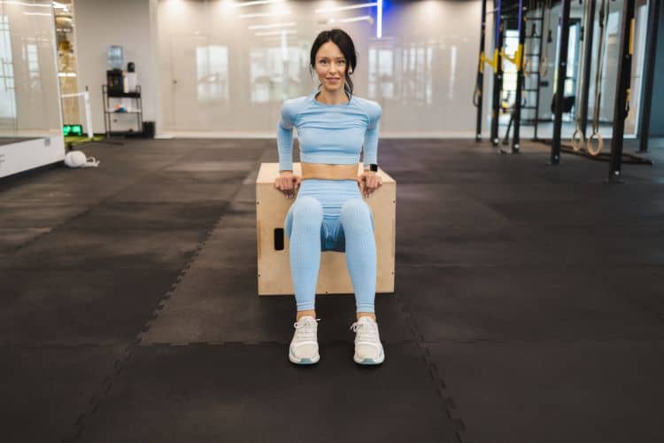 Woman performing tricep dips during a 30-minute no-weights upper body workout at a gym.