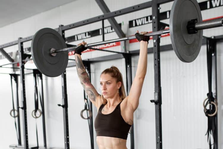 Woman pressing a barbell overhead in a gym during a 35 minute barbell strength training.