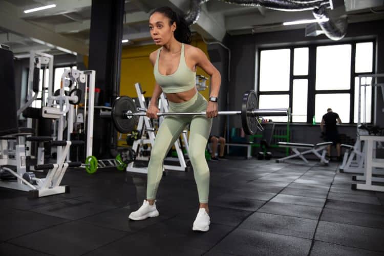 Woman performing barbell bent over rows during a 5 day full body barbell workout routine in the gym.