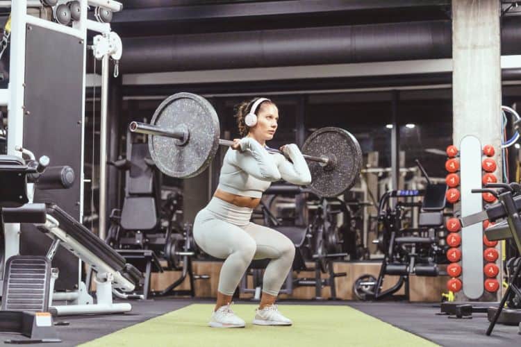 Woman performing a barbell squat during a 45-minute full body strength workout in a gym.