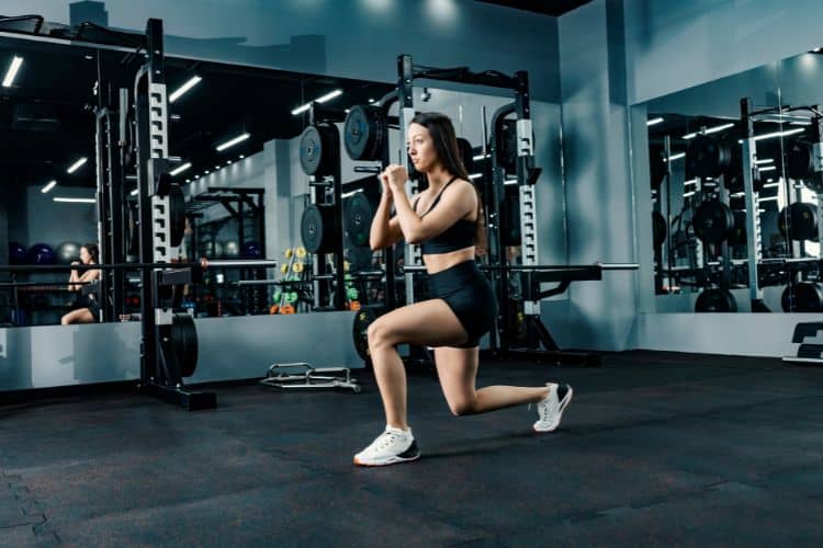 Woman doing a bodyweight lunge during a 30 minute no equipment workout at a gym.