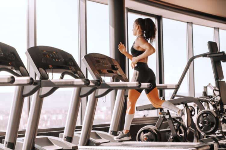 Woman performing a high-intensity sprint on a curved manual treadmill during a 20-minute HIIT workout, sweat flying.