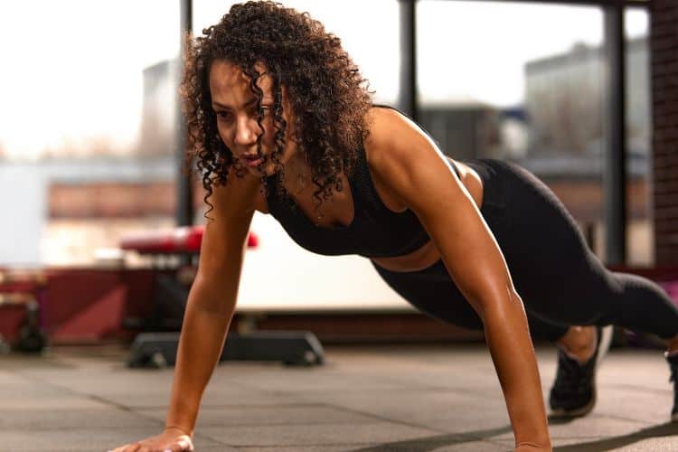 Woman in athletic wear preparing to do a burpee, starting in a squat position with hands on the floor for a 30-minute burpee fat loss workout.