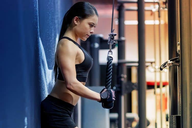 Person performing 25 minute cable machine tricep pushdown workout with rope attachment, standing at cable machine with elbows tucked and arms fully extended.