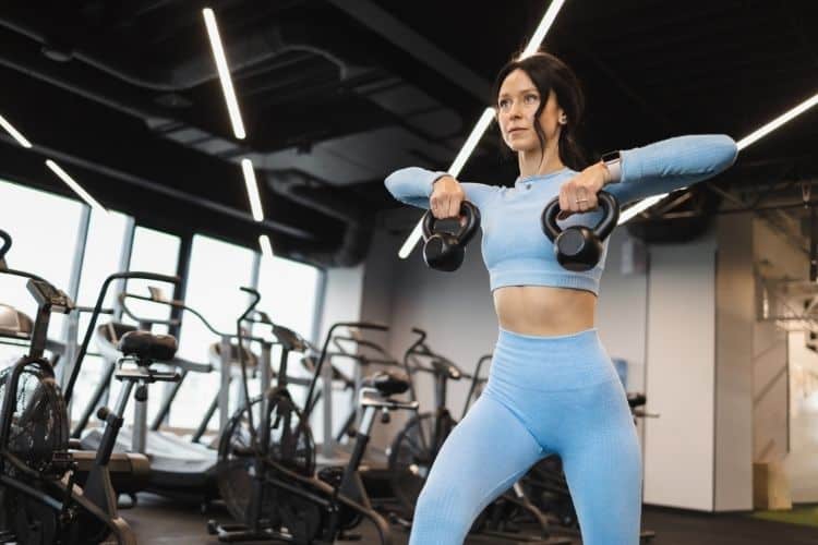 A woman holding two kettlebells with determination, representing an advanced 60-minute HIIT workout routine.