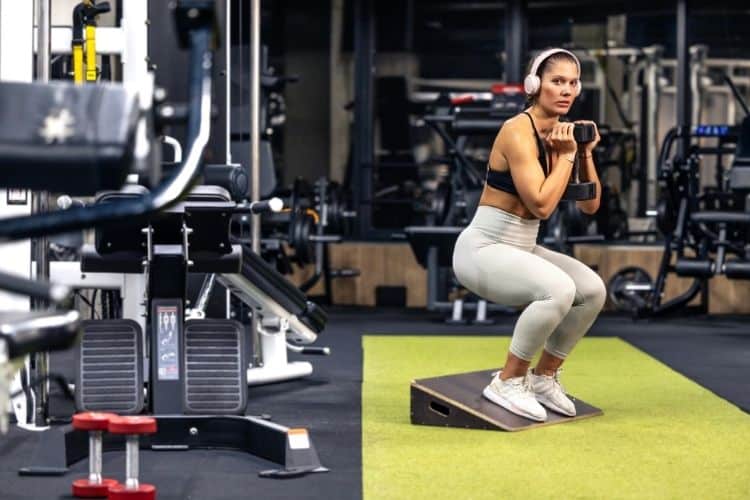 Woman doing a Goblet squat with a dumbbell for a unilateral leg exercise during a 35-min full body dumbbell superset workout routine.