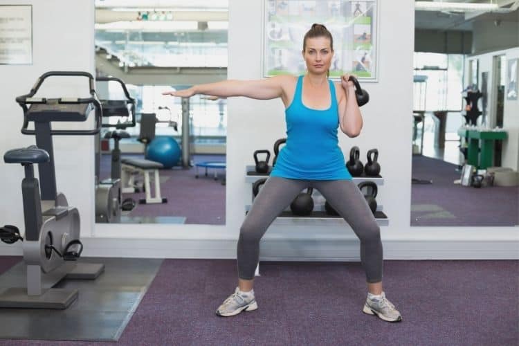 Woman performing kettlebell squat during a 20-minute HIIT ladder workout.