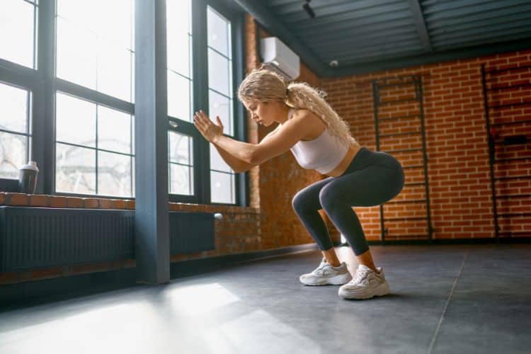 Woman performing a high-intensity jump squat in a living room for a 20-minute holiday damage control workout.