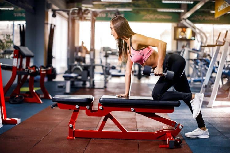 Woman doing dumbbell row in the gym as part of a 6-day splitlean strength workout upper body day routine.