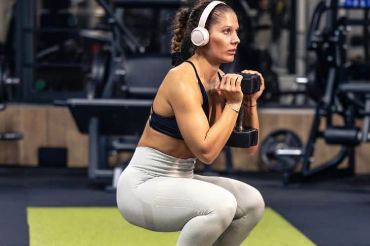 Woman performing a dumbbell squat during a 30-minute full body workout at a gym.