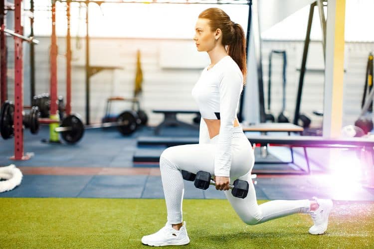 Woman performing dumbbell lunges in a gym during a 35-minute full body dumbbell workout.