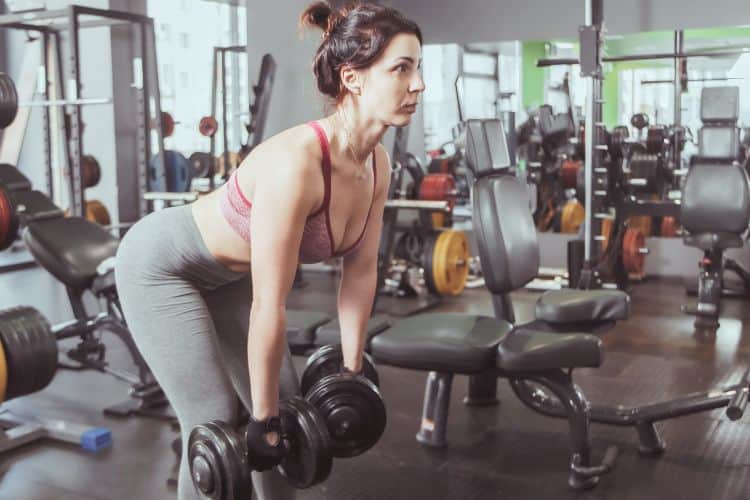 Woman performing deadlift for a 30-minute full body dumbbell tempo workout in a gym.