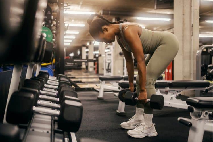 Woman performing Romanian deadlifts with dumbbells, focusing on hamstring stretch during a 15 minute dumbbell full body workout.