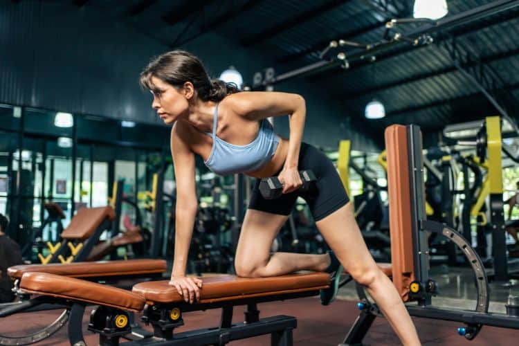 Woman performing dumbbell row during a 45-minute full body dumbbell workout at a gym.