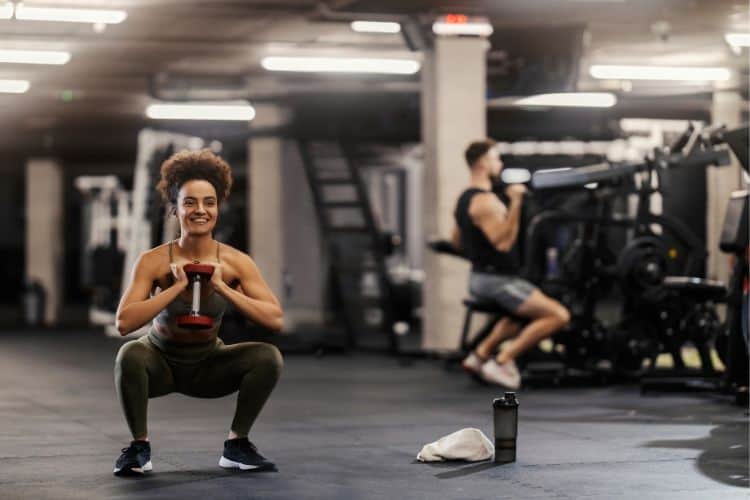Woman performing a dumbbell squat during 20 minute full body dumbbell workout in a gym.